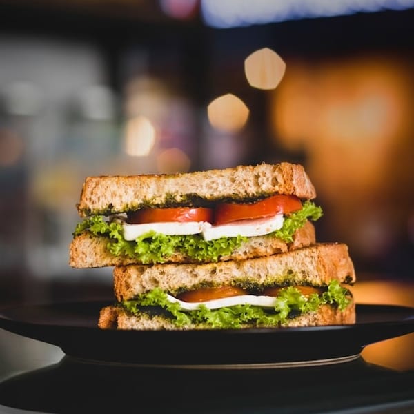 Two halves of a pesto, mozzarella, tomato, and lettuce sandwich on a dark plate.