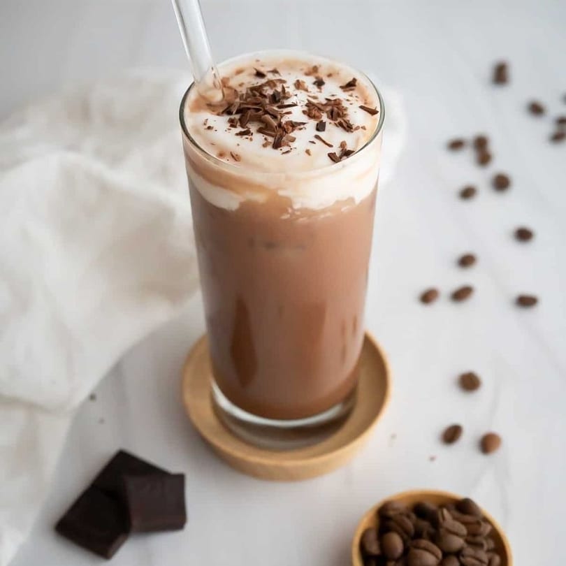 Iced mocha with whipped cream and chocolate shavings, coffee beans, and chocolate chunks.