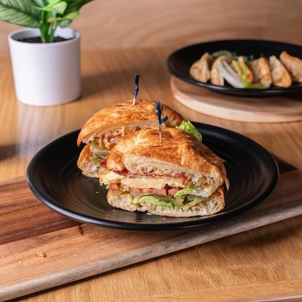 A croissant sandwich, iced matcha latte, and dumplings on a wooden table.