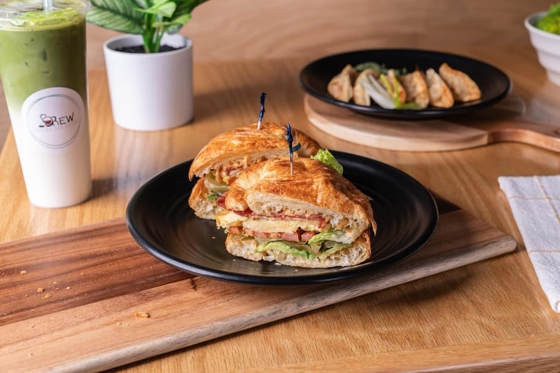 A croissant sandwich, iced matcha latte, and dumplings on a wooden table.