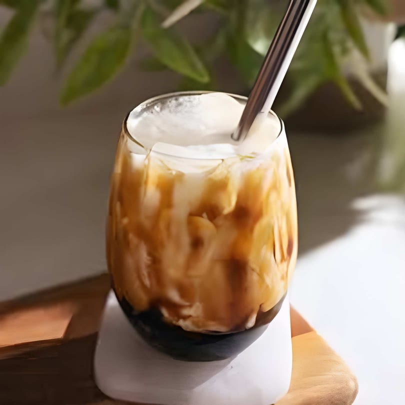 A glass of brown sugar boba tea with a metal straw, topped with creamy foam.