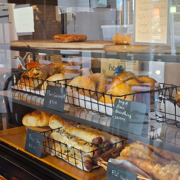 A bakery display case filled with various pastries, including croissants, bagels, and bagel dogs.