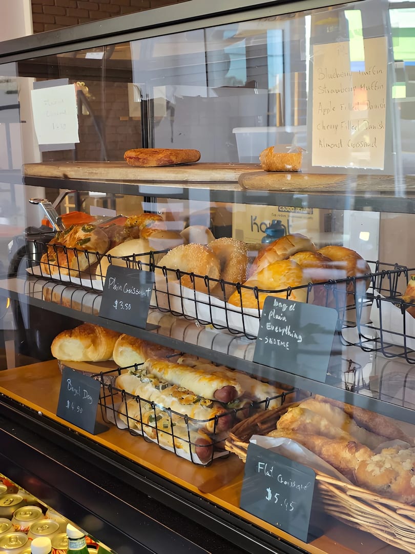 A bakery display case filled with various pastries, including croissants, bagels, and bagel dogs.
