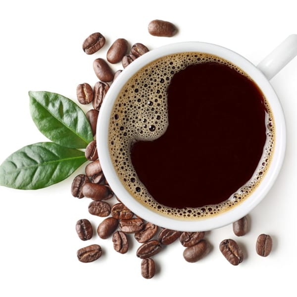 Overhead view of a white cup of black coffee with coffee beans and green leaves.